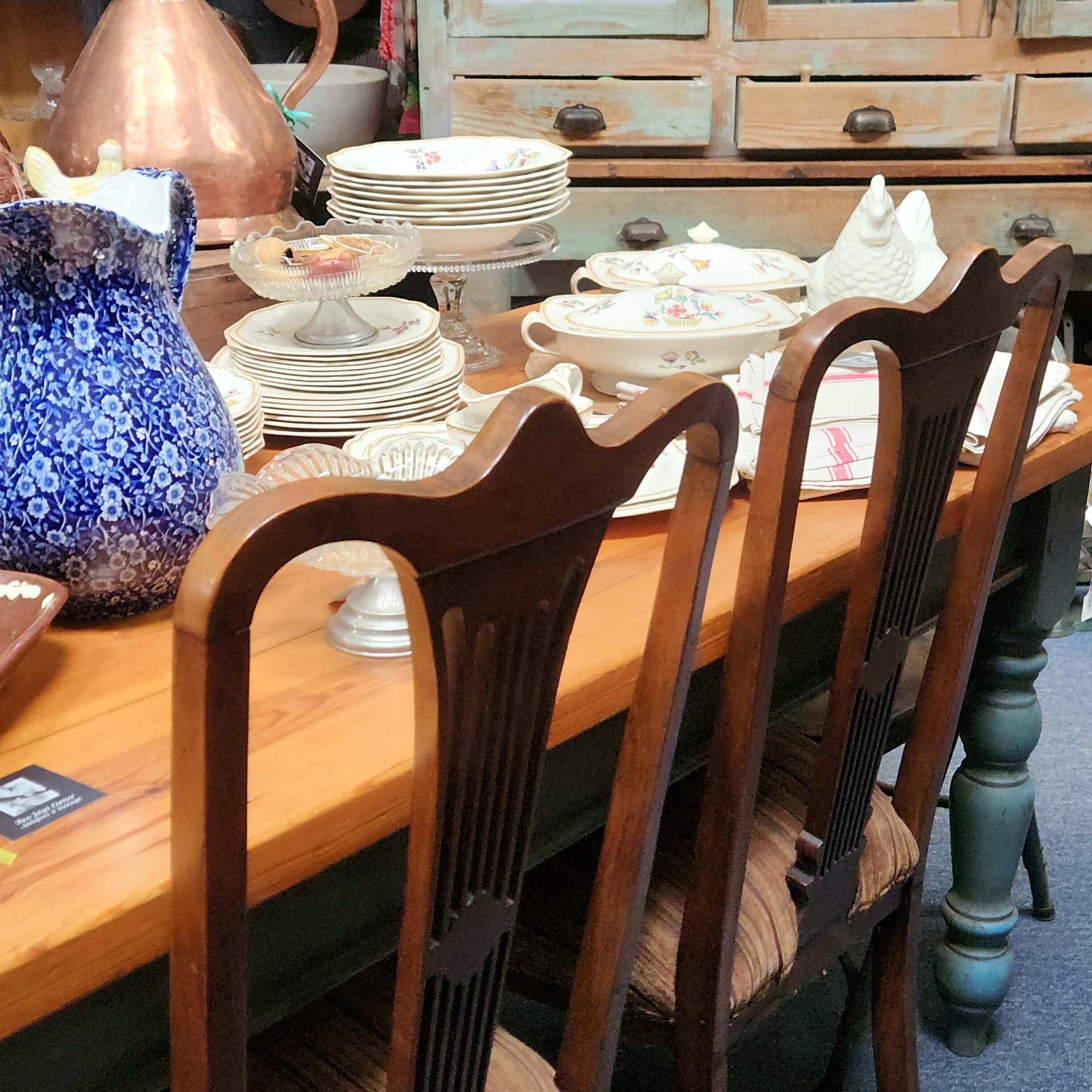 Table
                      and chairs with dinner service on top with a
                      dresser in the background